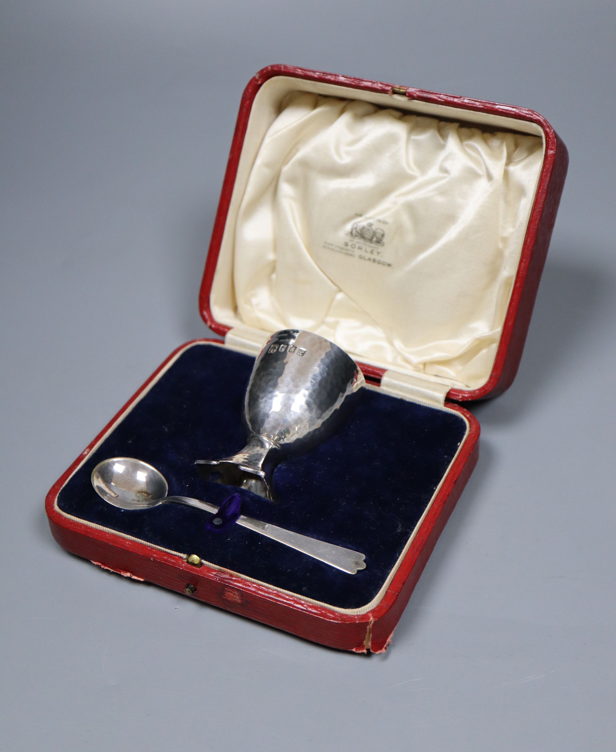 A cased Edwardian Art Nouveau silver egg cup and similar plated egg spoon, R & W Sorley, Glasgow, 1908, 67mm, 55 grams,